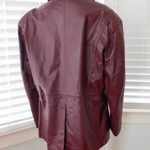 May include: A burgundy leather jacket with a long, fitted style. The jacket has a collar and a button closure.