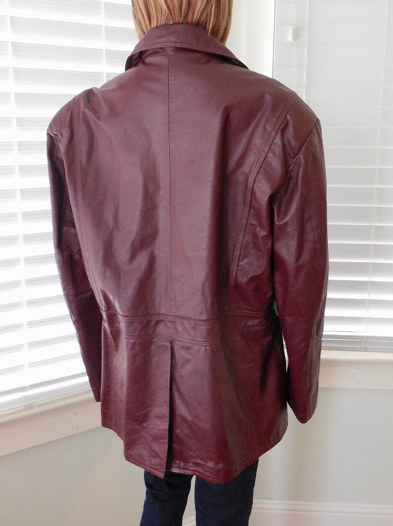 May include: A burgundy leather jacket with a long, fitted style. The jacket has a collar and a button closure.