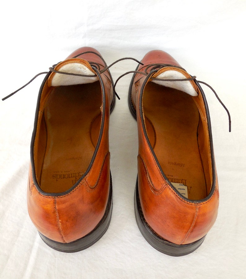 May include: A pair of brown leather dress shoes with dark brown laces. The shoes have a classic design with a rounded toe and a dark sole. The interior of the shoes is visible, showing a light-colored lining and the brand name.