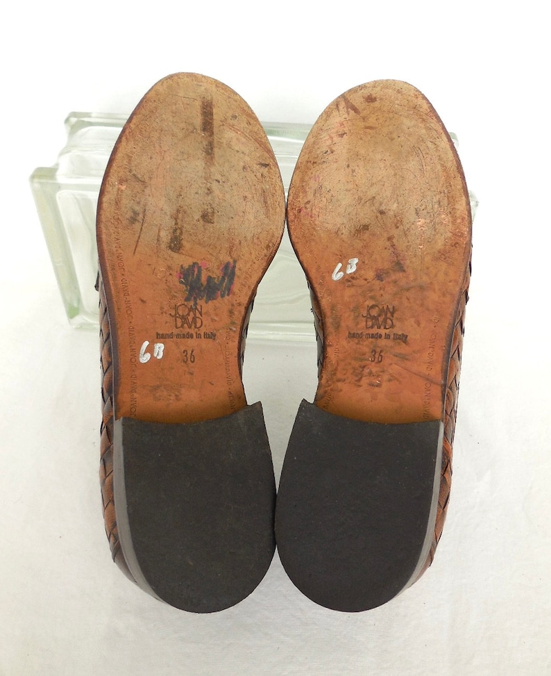 May include: Brown leather woven shoes with black soles. The shoes have the text "John David" and "hand-made in Italy" on the soles. The size is marked as "36" and "68" on the soles.