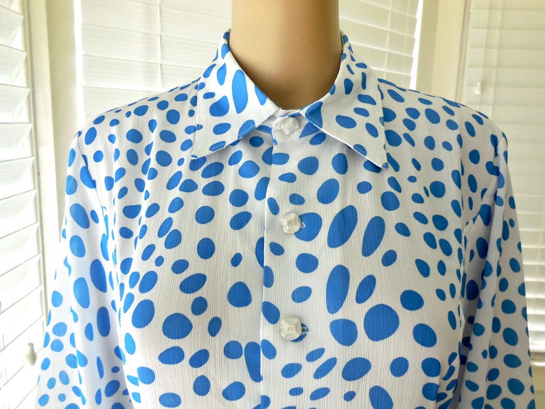 May include: White shirt with a blue polka dot pattern. The shirt features a classic collar and buttoned cuffs. The buttons are white and the fabric appears to be lightweight. The shirt is a classic design.