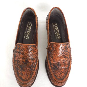 May include: A pair of brown leather loafers with a woven pattern. The loafers are handmade in Italy and have the brand name "Joan & David" printed on the inside.
