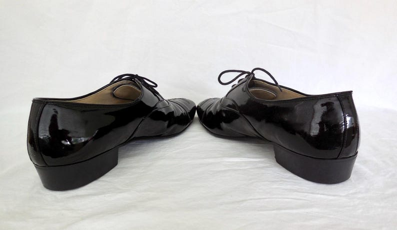 Puede incluir: Par de zapatos negros de charol con tac&oacute;n bajo y cierre de cordones. Los zapatos tienen un acabado brillante y un dise&ntilde;o cl&aacute;sico, adecuado para diversas ocasiones. Los tacones miden aproximadamente 2,5 cm.