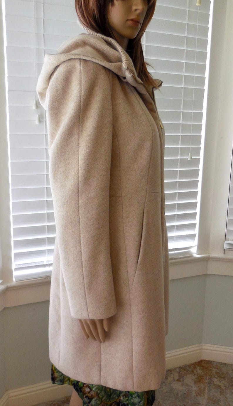 May include: A light beige hooded coat with a tailored fit. The coat features a hood, long sleeves, and a knee-length hem. The coat is made of a soft, textured fabric and has a classic, timeless design. A versatile outerwear piece.