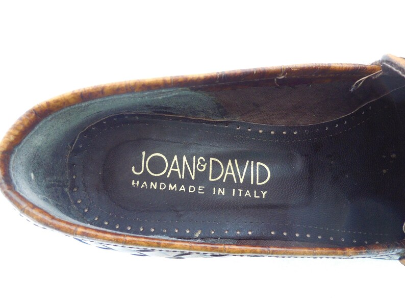 May include: Close-up of the inside of a brown leather loafer with a gold embossed label that reads "Joan & David Handmade in Italy."