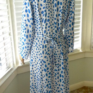 May include: A long-sleeved, knee-length dress with a white background and a pattern of blue polka dots. The dress has a tie belt at the waist and a collared neckline. The dress is made of a lightweight fabric.