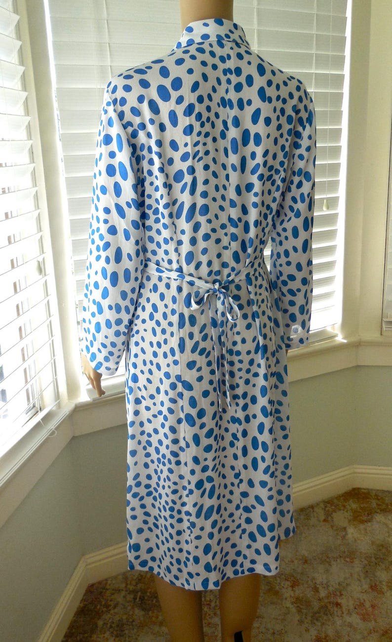 May include: A long-sleeved, knee-length dress with a white background and a pattern of blue polka dots. The dress has a tie belt at the waist and a collared neckline. The dress is made of a lightweight fabric.
