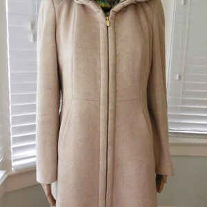 May include: A beige hooded coat with a full-length zipper. The coat has a tailored fit, long sleeves, and a high collar. The hood is a lighter shade of beige. The coat is displayed on a mannequin.
