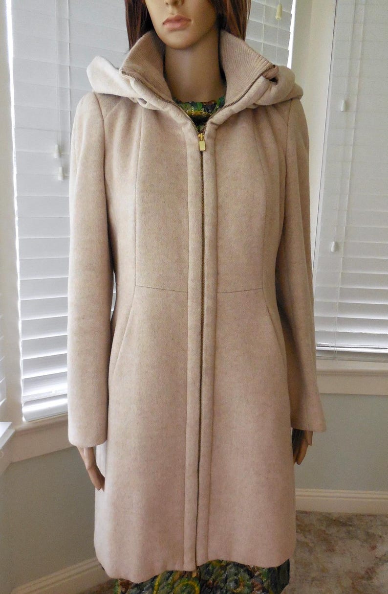 May include: A beige hooded coat with a full-length zipper. The coat has a tailored fit, long sleeves, and a high collar. The hood is a lighter shade of beige. The coat is displayed on a mannequin.