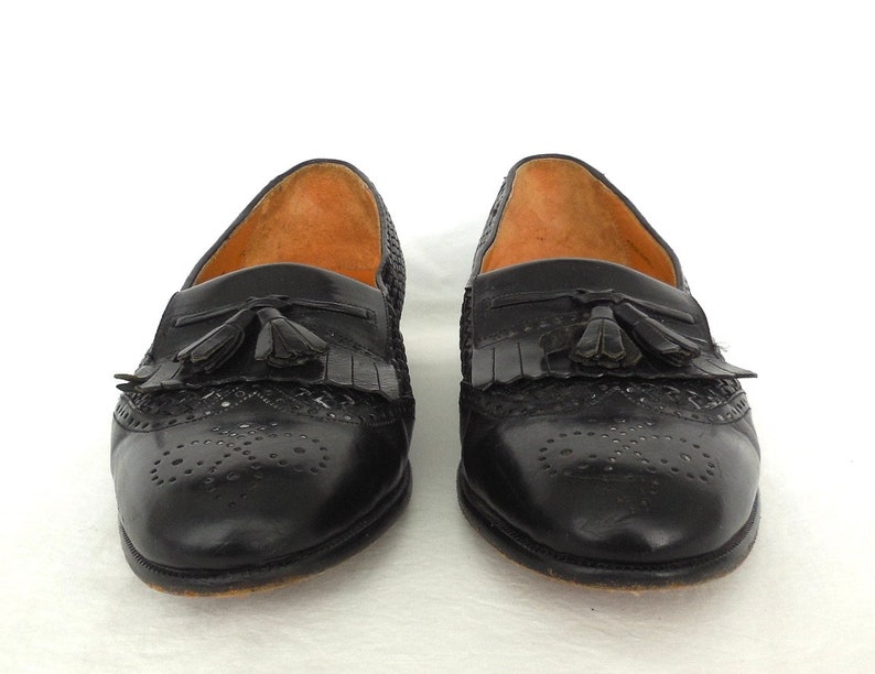 May include: A pair of black leather tassel loafers with a woven pattern and perforated detailing.