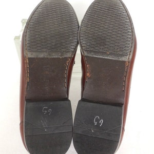 K&ouml;nnte beinhalten: Ein Paar braune Lederschuhe mit schwarzer Gummisohle. Die Sohlen sind mit der Nummer "69" gekennzeichnet.