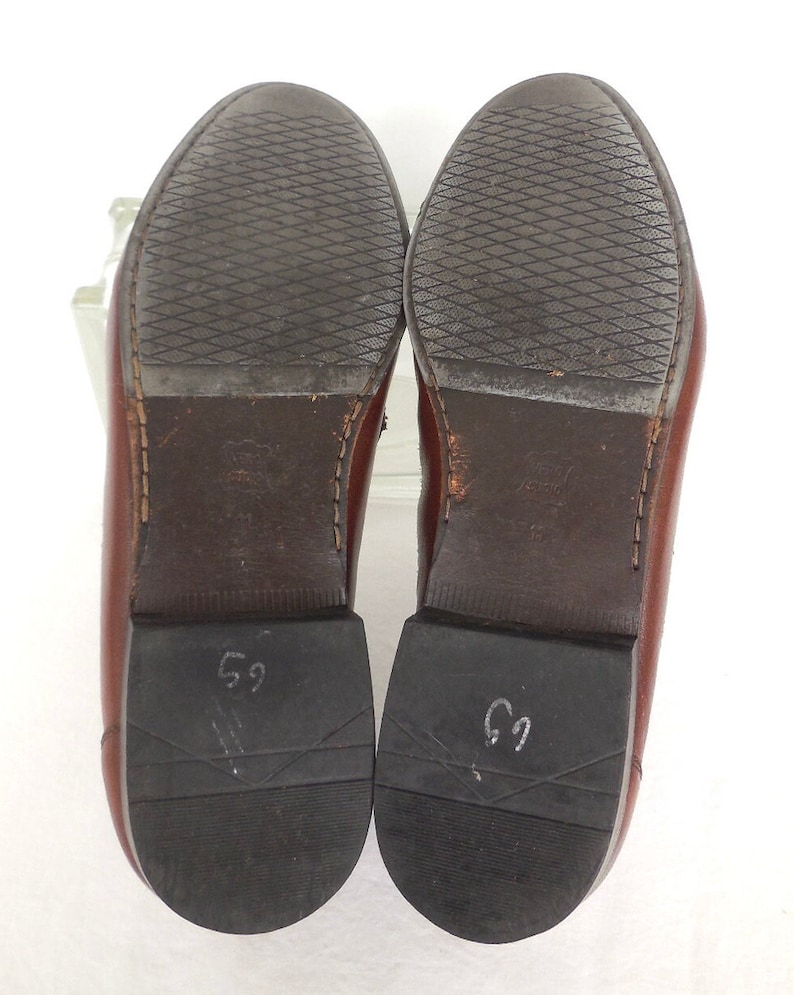K&ouml;nnte beinhalten: Ein Paar braune Lederschuhe mit schwarzer Gummisohle. Die Sohlen sind mit der Nummer "69" gekennzeichnet.