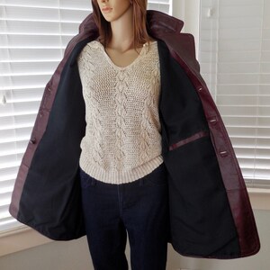 May include: A burgundy leather jacket with a black lining and a button closure. The jacket is open and the lining is visible.