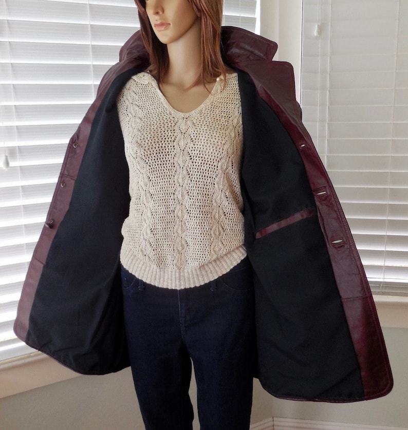 May include: A burgundy leather jacket with a black lining and a button closure. The jacket is open and the lining is visible.