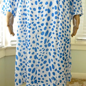 May include: A white dress featuring a blue polka dot design. The dress has long sleeves and a button-up front. The knee-length dress is made of a lightweight material, suitable for warmer weather.