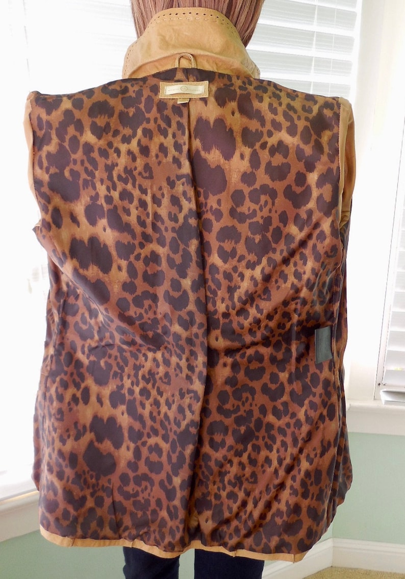 May include: A brown leather jacket with a leopard print lining. The jacket has a zipper closure and a collar.