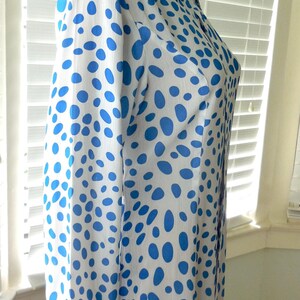 May include: A white dress featuring a blue polka dot design. The dress has long sleeves and a collared neckline. The fabric appears lightweight, and the dress is buttoned down the front. The dress is displayed on a mannequin.
