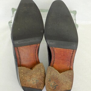 Puede incluir: Primer plano de las suelas de dos zapatos de cuero negro. Los zapatos tienen plantillas de cuero marr&oacute;n y est&aacute;n marcados con el texto "GOOD YEAR" y "GOODYEAR".