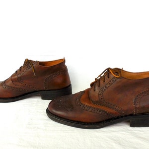 Pode incluir: Um par de botas de tornozelo de couro marrom com fecho de cadar&ccedil;o. As botas t&ecirc;m um padr&atilde;o decorativo de pequenos furos e costuras.