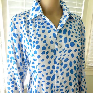 May include: A white shirt with a pattern of blue oval shapes. The long-sleeved shirt has a collar and is buttoned up the front with clear buttons. The shirt is made of a lightweight fabric.