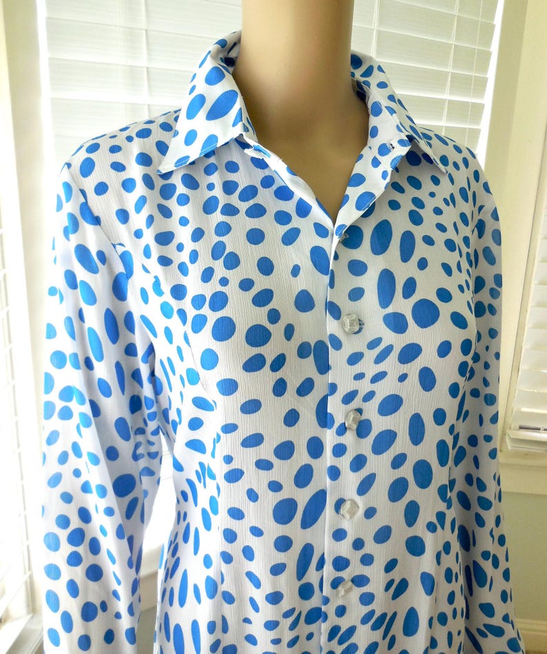 May include: A white shirt with a pattern of blue oval shapes. The long-sleeved shirt has a collar and is buttoned up the front with clear buttons. The shirt is made of a lightweight fabric.