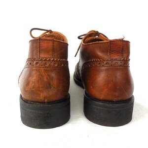 Pode incluir: Um par de sapatos de couro marrom com sola preta. Os sapatos t&ecirc;m fecho de atacadores e um design de ponta de asa.