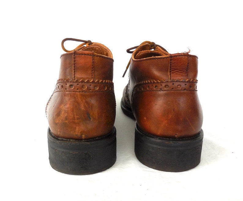 Pode incluir: Um par de sapatos de couro marrom com sola preta. Os sapatos t&ecirc;m fecho de atacadores e um design de ponta de asa.