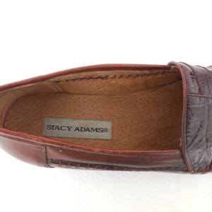 K&ouml;nnte beinhalten: Brauner Leder-Slipper mit gen&auml;htem Rand und einem Obermaterial aus krokodilgepr&auml;gtem Leder. Der Slipper tr&auml;gt ein Etikett mit der Aufschrift "Stacy Adams".