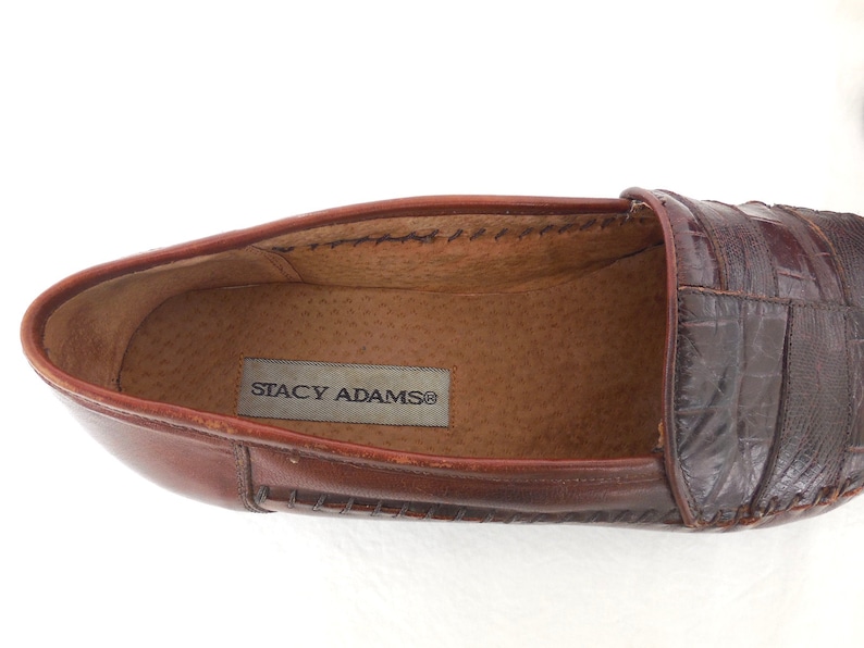 K&ouml;nnte beinhalten: Brauner Leder-Slipper mit gen&auml;htem Rand und einem Obermaterial aus krokodilgepr&auml;gtem Leder. Der Slipper tr&auml;gt ein Etikett mit der Aufschrift "Stacy Adams".