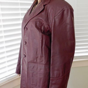 May include: A burgundy leather jacket with a button-up front and two pockets. The jacket has a collar and long sleeves.