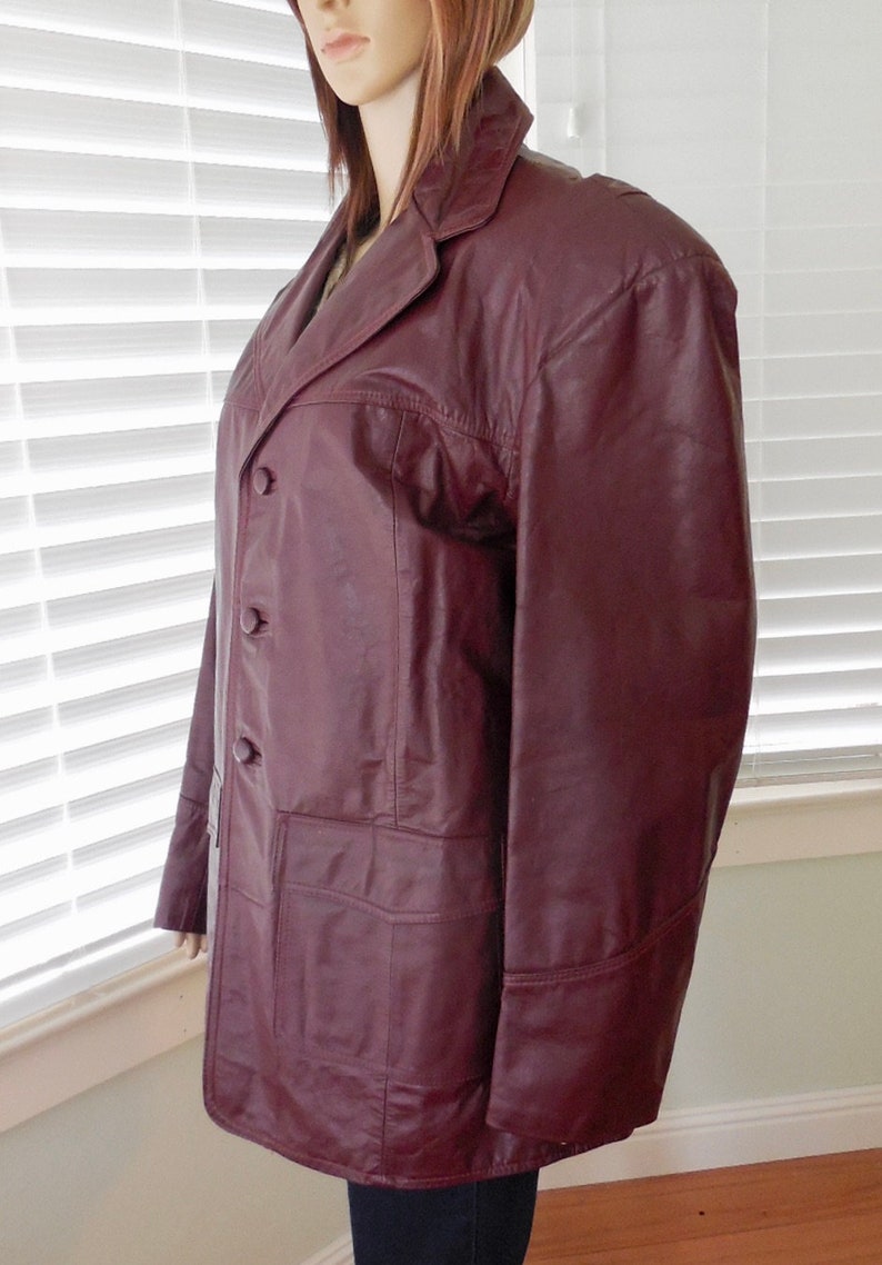 May include: A burgundy leather jacket with a button-up front and two pockets. The jacket has a collar and long sleeves.