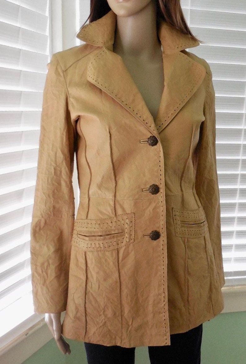 May include: A tan leather jacket with decorative stitching and three buttons. The jacket has a collar and long sleeves.