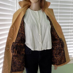 May include: A tan leather jacket with a leopard print lining. The jacket has a button closure and pockets.