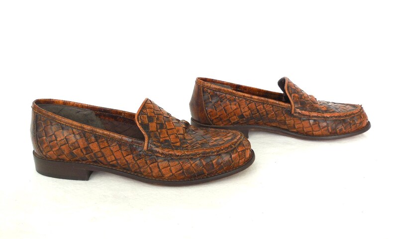 May include: A pair of brown leather woven loafers. The loafers have a woven pattern and a pointed toe.