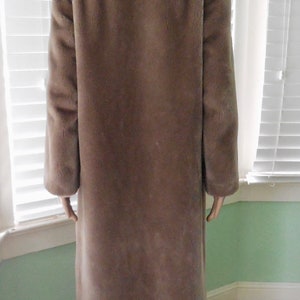 May include: A long, brown faux fur coat with a large collar. The coat is made of a soft, plush fabric and has a relaxed fit.