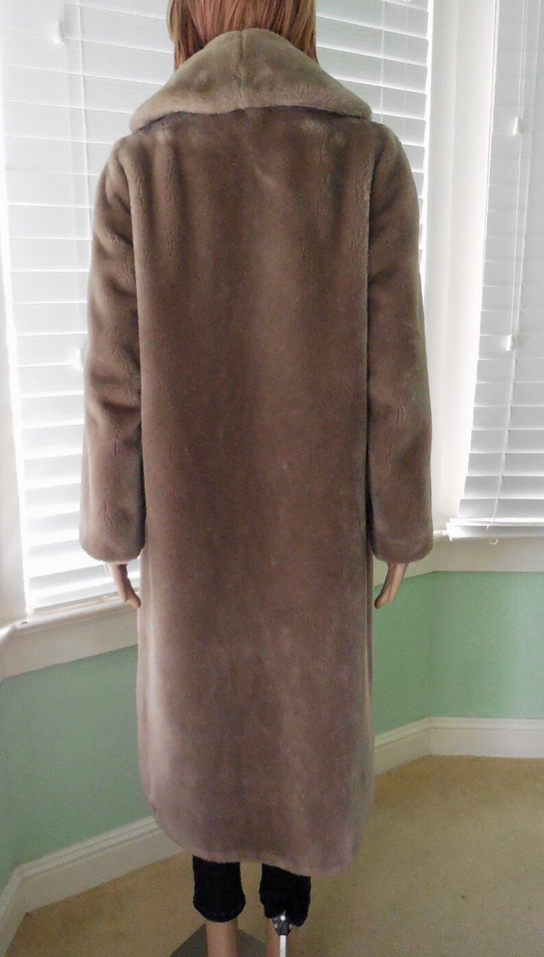 May include: A long, brown faux fur coat with a large collar. The coat is made of a soft, plush fabric and has a relaxed fit.