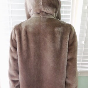 May include: A long-sleeved, light brown faux fur jacket with a high collar and a hood.