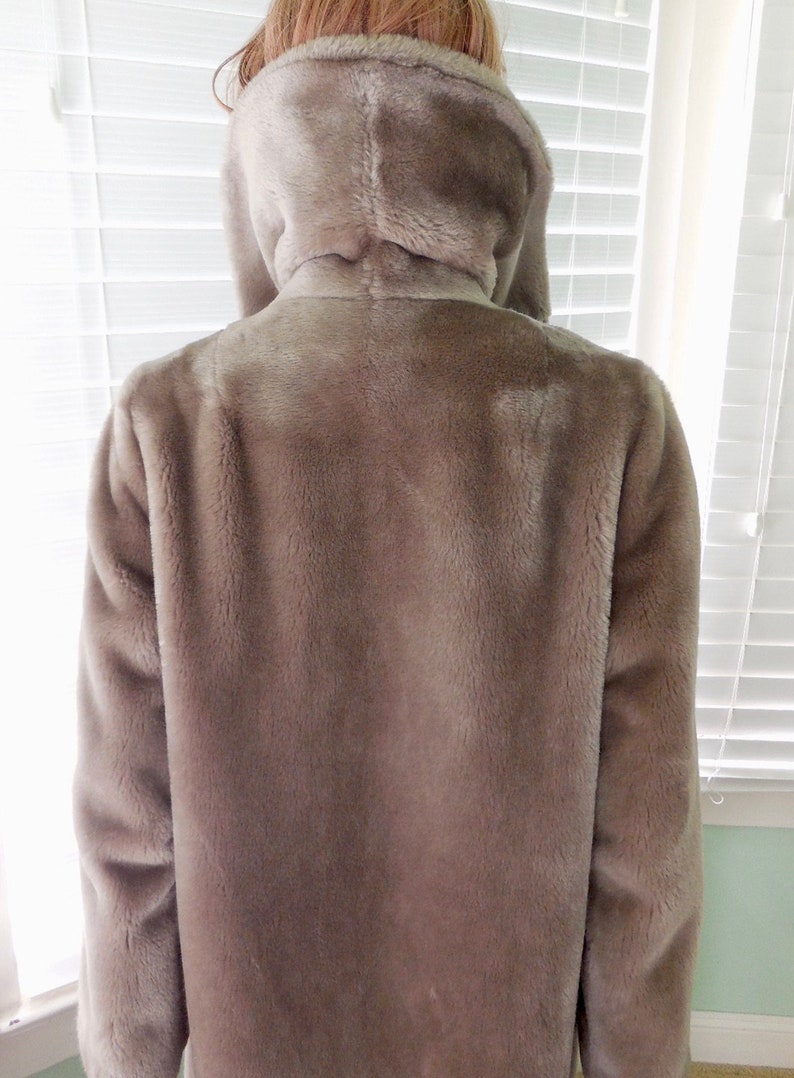 May include: A long-sleeved, light brown faux fur jacket with a high collar and a hood.