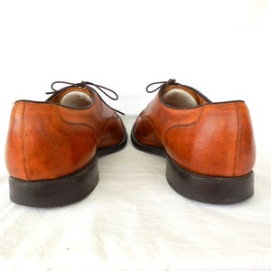 May include: A pair of brown leather dress shoes with dark brown soles and laces. The shoes are displayed against a white background, showcasing their classic design and craftsmanship. The leather has a rich, warm tone.