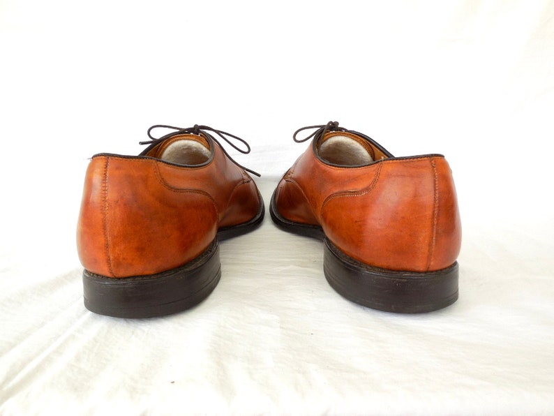 May include: A pair of brown leather dress shoes with dark brown soles and laces. The shoes are displayed against a white background, showcasing their classic design and craftsmanship. The leather has a rich, warm tone.