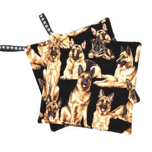 May include: Two black oven mitts with a repeating pattern of German Shepherds in various poses. The mitts have a quilted design and a black loop with white paw prints for hanging.
