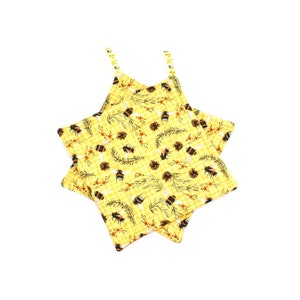 May include: Two yellow fabric coasters with a bee and floral pattern. The coasters have a gingham background with images of bees, flowers, and pinecones. The straps are decorated with small yellow flowers.