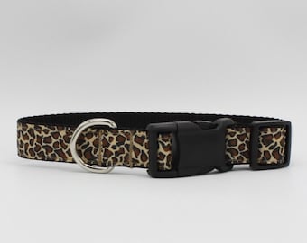 May include: A dog collar with a black plastic buckle and a silver-colored metal D-ring. The collar features a leopard print pattern in shades of brown and tan against a black background. The collar is designed for pets.