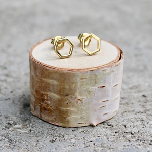 May include: A pair of gold hexagon stud earrings on a small wooden stand.