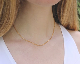May include: A delicate gold chain necklace worn by a person with long blonde hair. The chain is thin and has a subtle shimmer.