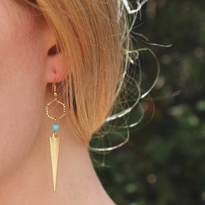 May include: Gold earrings with a turquoise bead and a geometric hexagon shape. The earrings have a long, pointed drop.