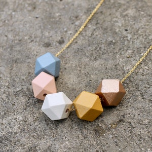 May include: A gold chain necklace with six geometric wooden beads in shades of blue, pink, white, and gold.
