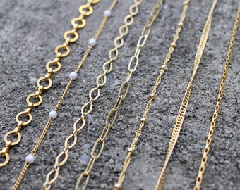 May include: A collection of seven gold chains of varying styles and thicknesses. Some chains feature small white beads.