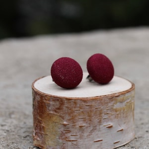 Peut inclure: Une paire de boucles d'oreilles clous en tissu bordeaux sur un petit rondin de bouleau.