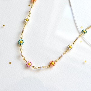 May include: A gold chain necklace with colorful flower charms. The flowers are pink, blue, yellow, and white.